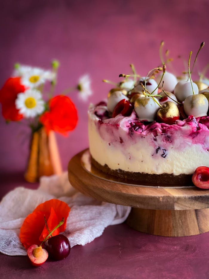 Delicious cherry cheesecake topped with gold cherries and flowers, perfect for celebrations.
